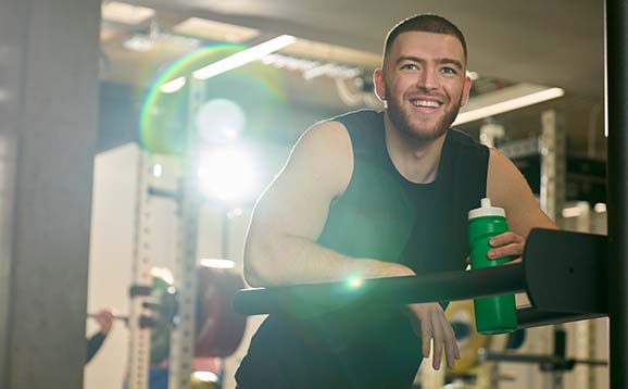 A smiling gym member drinking a bottle of water