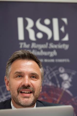man in a suit sitting in front of a banner that says rse
