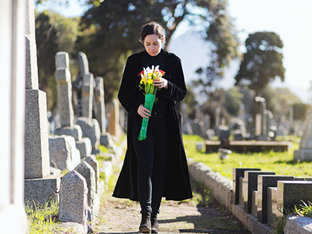 Woman walking through graveyard holding flowers