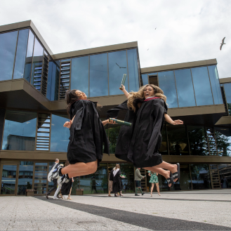 Two graduates jumping by Campus Central