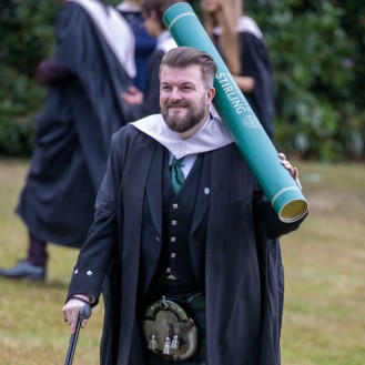 Male graduate poses with giant scroll prop