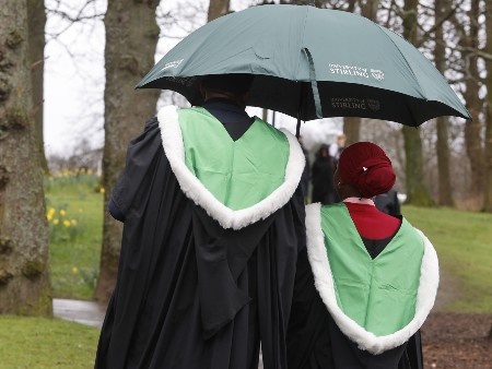 Two graduates pose with their backs to camera holding an umbrella