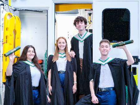 Ida, Roisin, Drew and Matthew pose in graduation gowns next to an ambulance