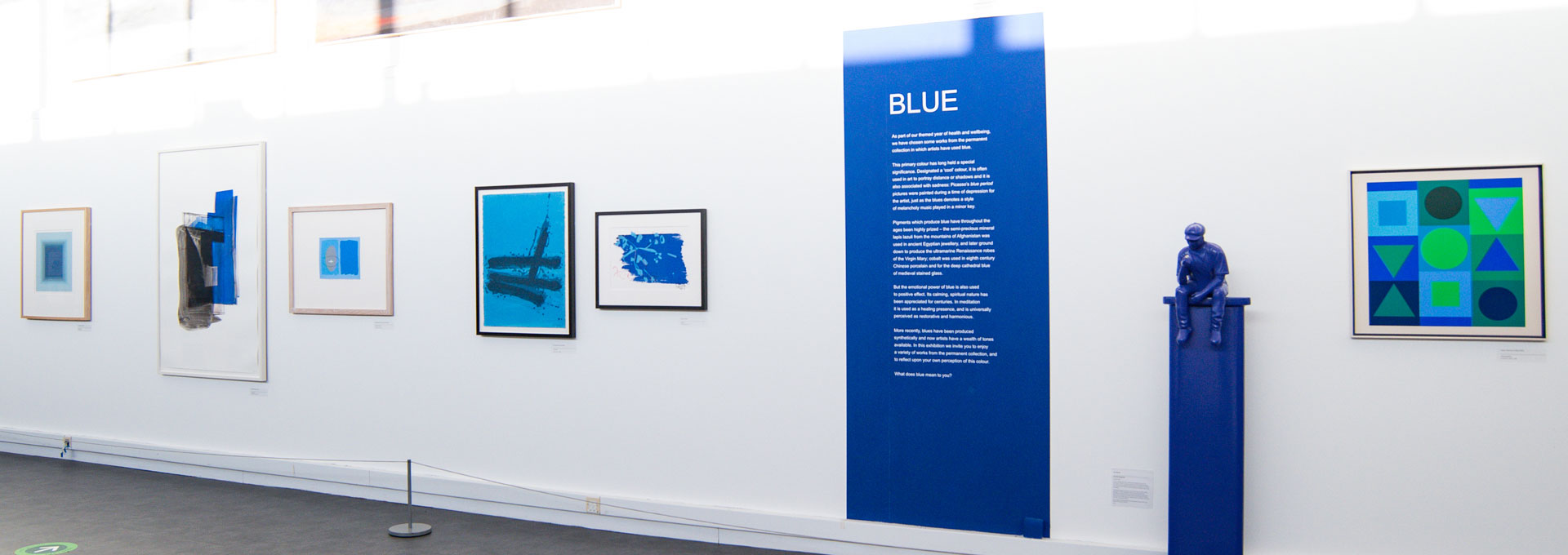 A white wall with artwork displayed on it and a blue sculpture
