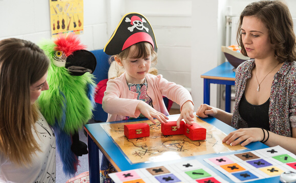 Two researchers, one with toy parrot, and child with pirate hat run an experiment