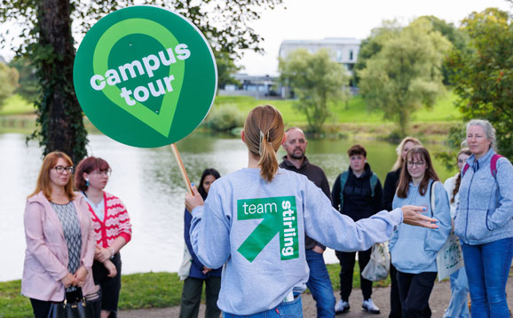 A student ambassador confidently leading a campus tour group around the scenic loch.