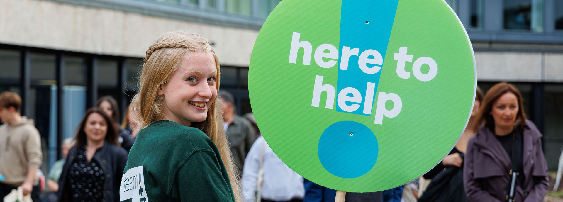 A student ambassador holding a 'here to help' sign