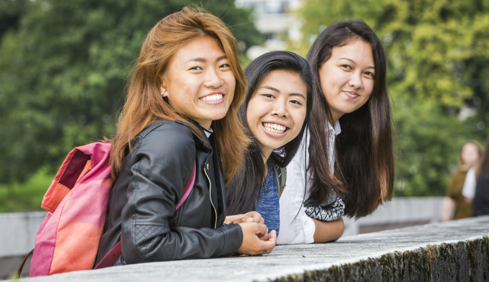 three students standing together on the loch bridge and smiling 