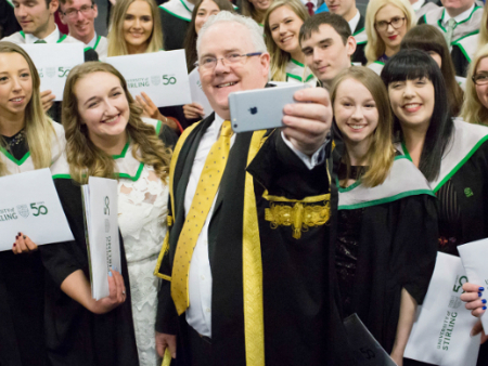recent graduates with smiles on their faces taking a selfie with stirlings principal 