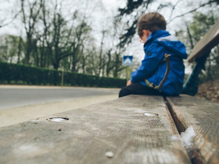 young child sitting alone on a bench beside a road