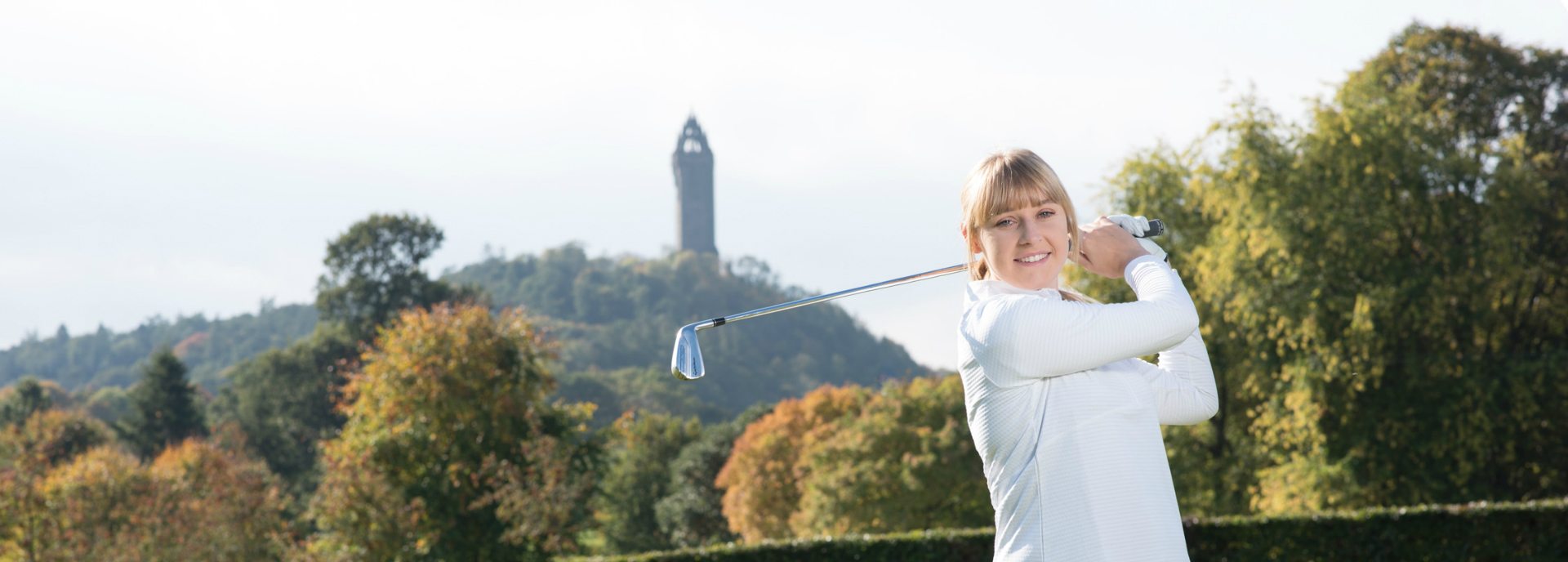 Nicola Slater swinging a golf club with Wallace Monument in background