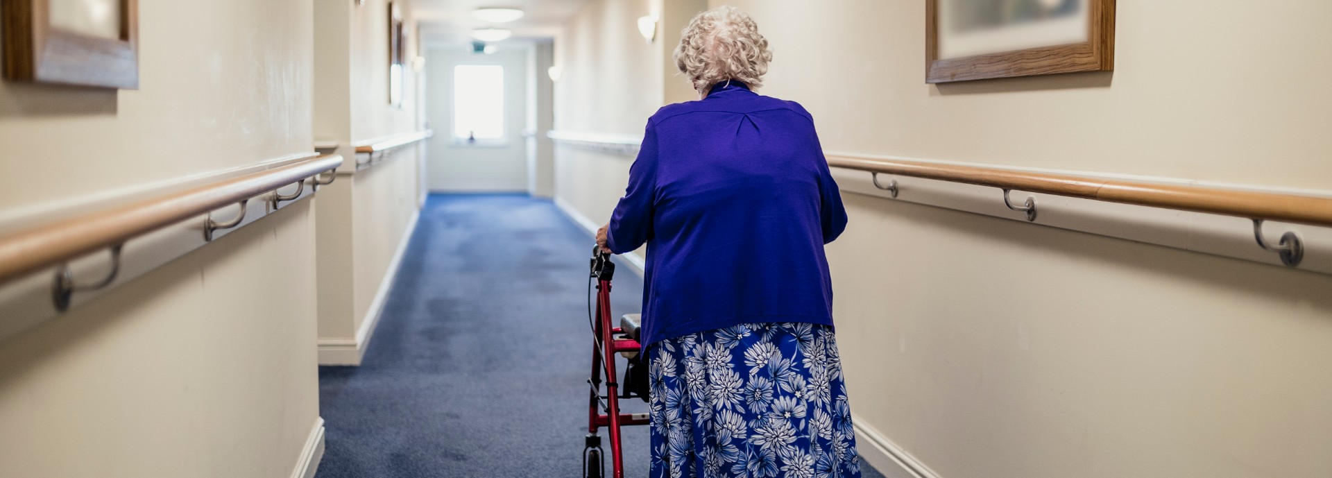 Elderly woman walks along hall using a walking frame