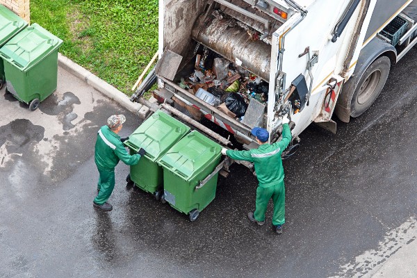 Two refuse workers loading green household bins on to a bin lorry
