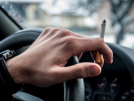 Image of driver's hand on wheel with cigarette