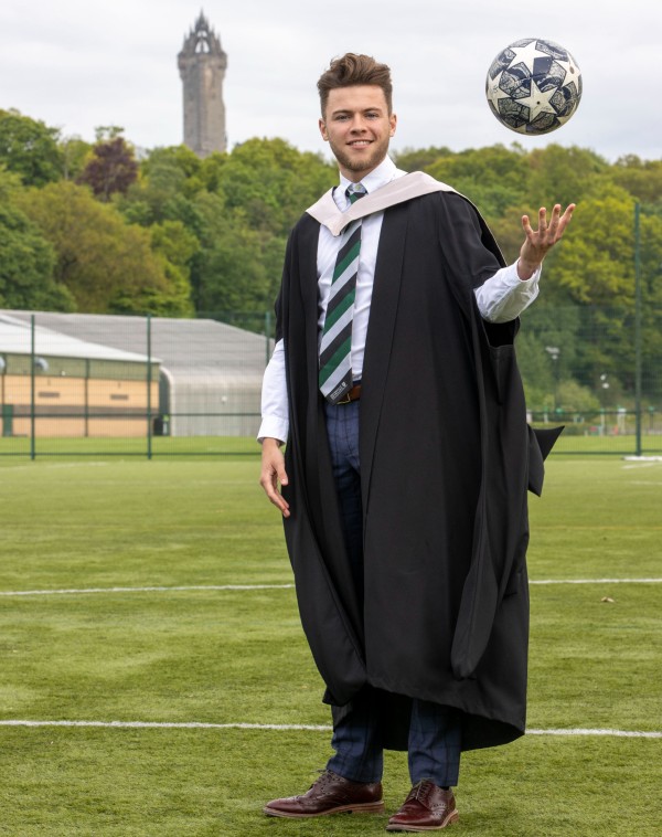 Craig Brown tosses football in the air, while wearing his graduation gown
