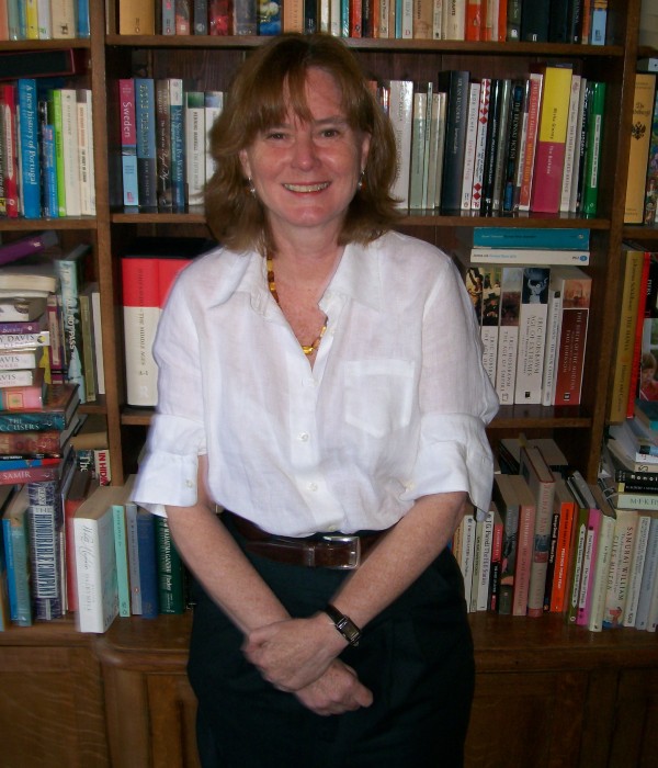 Prof Catherine Hennessy stands in front of a bookcase. She wears a white shirt and black trousers.