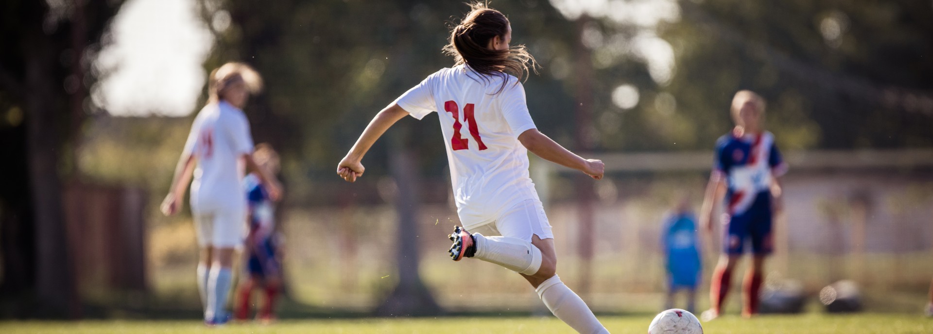 Girl wearing a white football strip shapes up to kick a football.