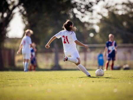Girl wearing a white football strip shapes up to kick a football.