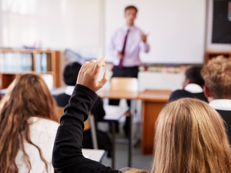 Stock photos of a classroom. A teacher stands in front of a whiteboard with students sitting at desks facing them.