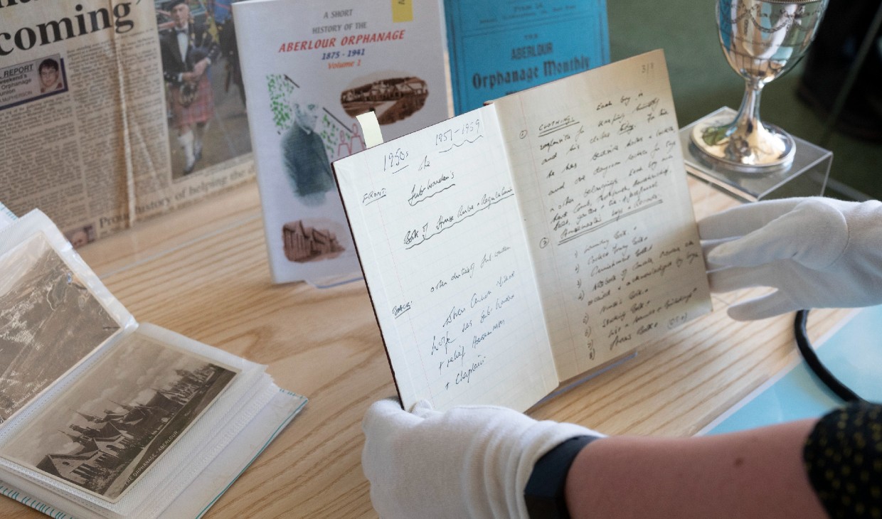 Items from the archive on a table with one old book opened and held by gloved hands