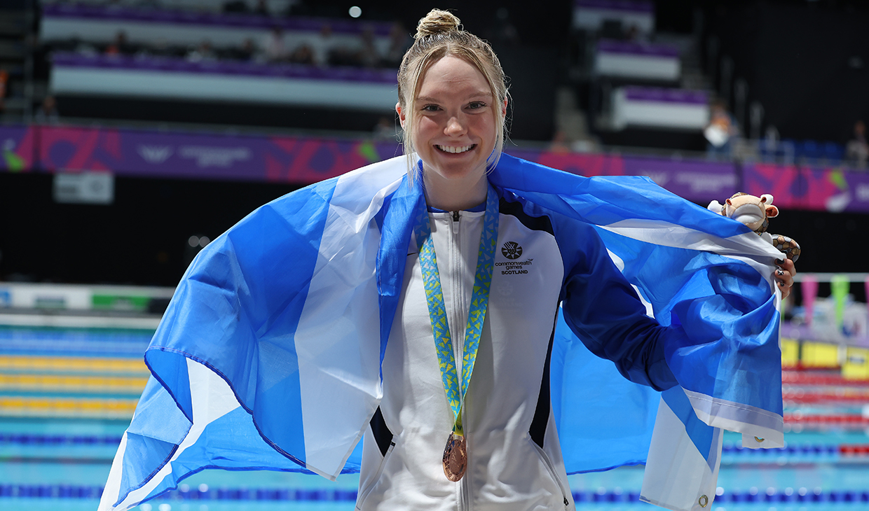 Toni Shaw with flag over shoulders wearing bronze medal