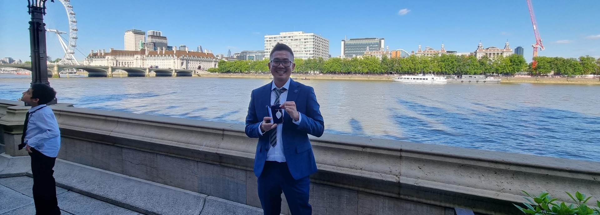 Nicolas Kee Mew stands in front of the River Thames, London holding his medal