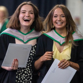 Two female graduations laughing dressed in graduation robes
