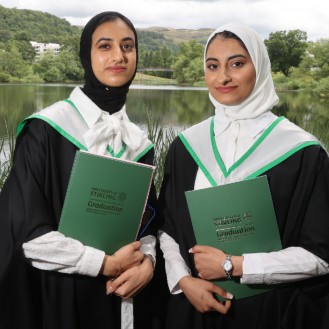 Two students pose in graduation gowns by the loch