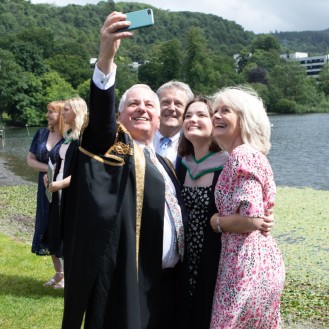 Chancellor poses with a family by loch after graduation