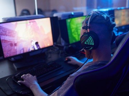 Rear view of young gamer wearing gaming headphones with backlight and playing in computer video game on computer