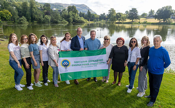 Group of people pose with banner in front of loch