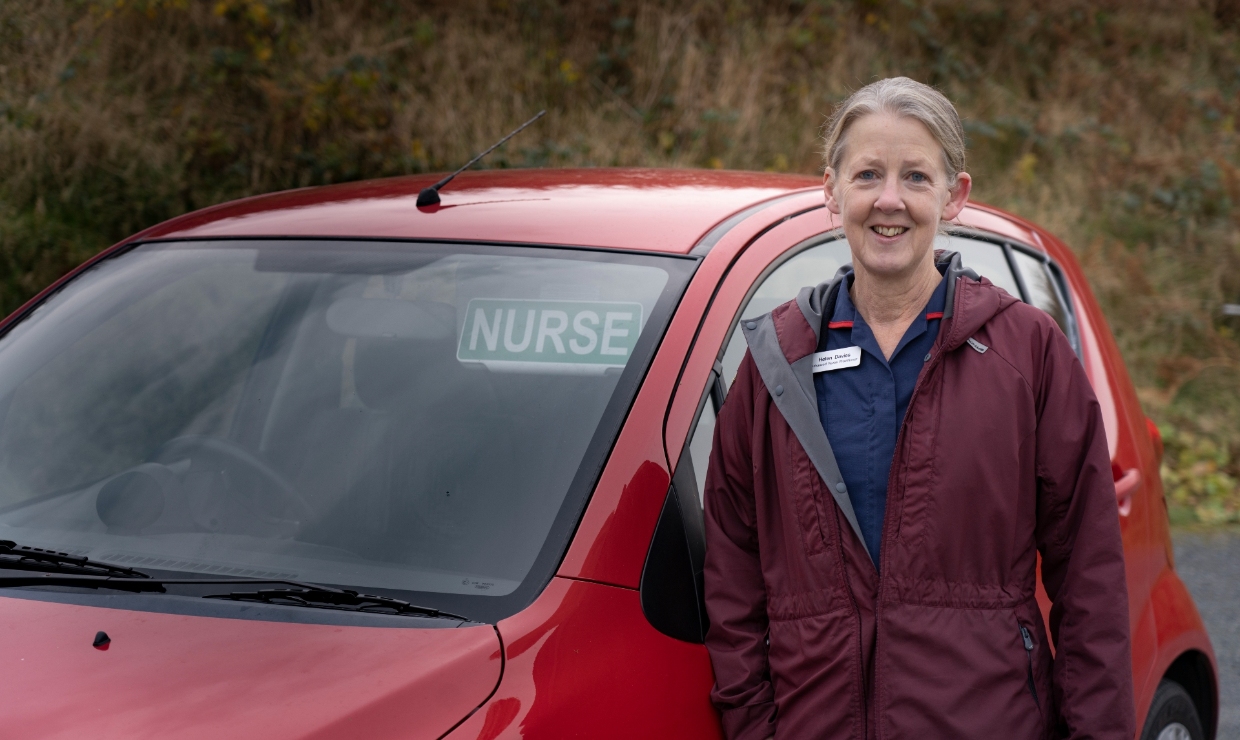 Nurse Helen Davies in her uniform beside her car which displays a sign saying 'Nurse' in the window