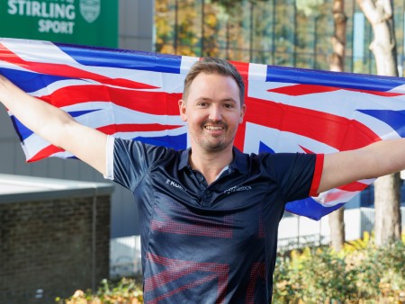 Paul Greaves holds a Great Britain flag outstretched above his head outside the University's Sports Centre