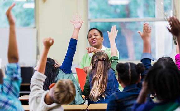 Children raise hands to teacher