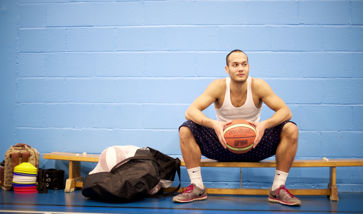 Basketball player stting in the sports hall holding a basketball