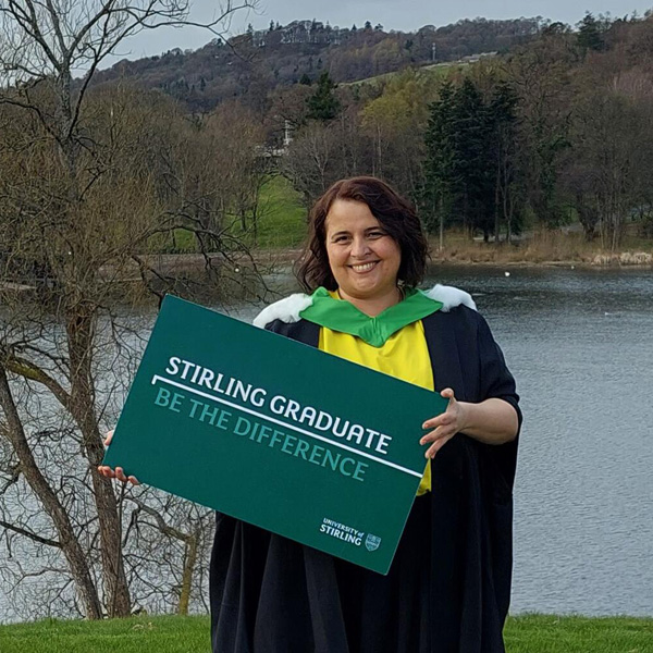 Alina by the loch holding a Stirling Graduate sign